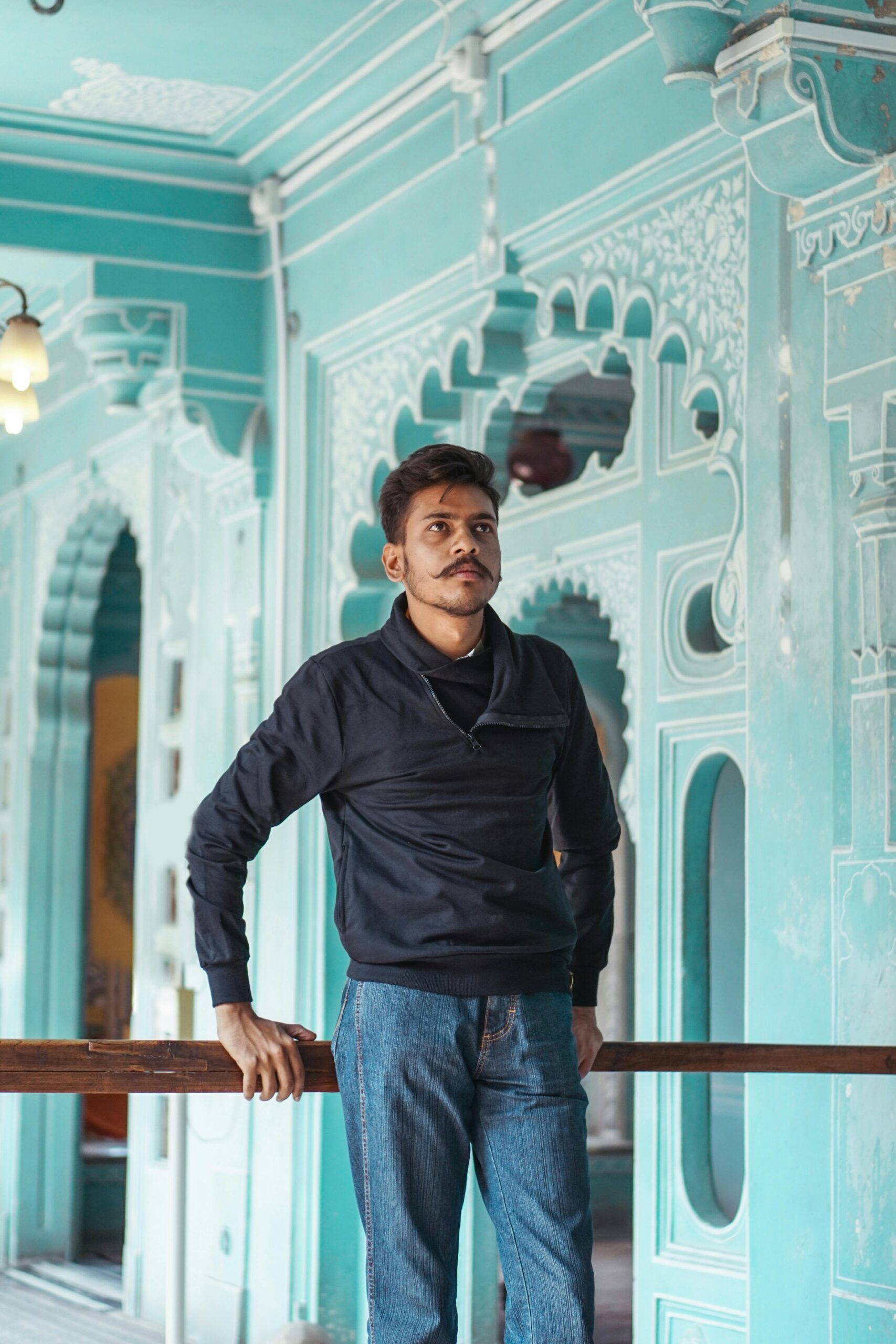A young man standing indoors against a backdrop of ornate historical architecture with intricate patterns.